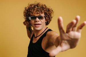 Fashionable curly young man in trendy glasses gesturing and smiling against yellow background photo