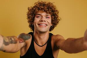 Portrait of handsome young gay man with make-up winking at camera against yellow background photo