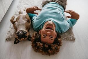 Top view of young man looking at camera and smiling while lying on the floor with his cute funny dog photo