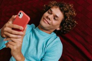 Top view of handsome young man using smart phone and smiling while lying on bed photo