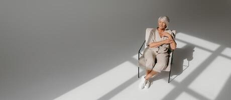Top view of calm gray hair senior woman relaxing in comfortable chair in sunny studio photo