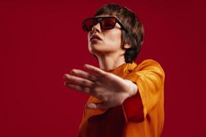 Attractive young short hair woman in trendy glasses stretching out hand against red background photo