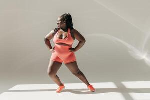 Full length of happy African plus size woman in sportswear warming up before training in fitness studio photo