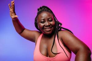 Joyful African plus size woman in sportswear gesturing and smiling against vibrant background photo