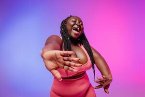 Beautiful African plus size woman in sportswear gesturing and smiling against vibrant background photo