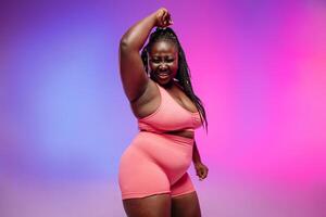 Joyful plus size woman in sportswear radiating self-love while dancing on vibrant background photo