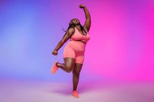 Full length of joyful curvy woman in sportswear dancing and smiling on colorful background photo