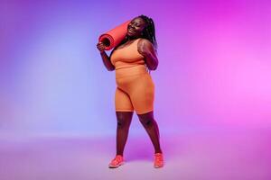 Active young voluptuous woman in sportswear carrying exercise mat and smiling on pink background photo