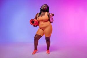 Active young voluptuous woman in sportswear carrying exercise mat and smiling on pink background photo