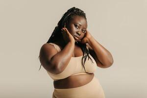 Beautiful curvy African woman in underwear touching face and looking at camera on studio background photo