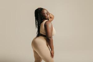 Side view of voluptuous young African woman in underwear radiating joy and self-love on studio background photo