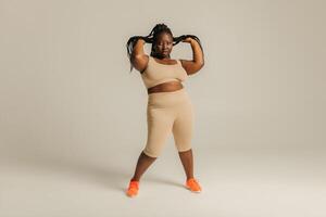Full Length of beautiful African plus size woman in sportswear adjusting her dreadlocs on studio background photo