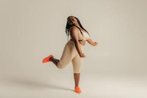 Full length happy plus size African woman in sportswear dancing on studio background photo