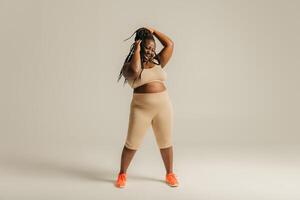 Full Length of beautiful African plus size woman in sportswear adjusting her dreadlocs on studio background photo