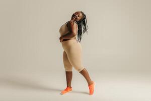 Happy plus size African woman in sportswear looking confident in her body while standing on studio background photo