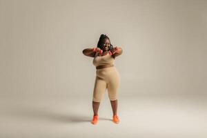 Full length happy plus size African woman in sportswear exercising with dumbbells on studio background photo