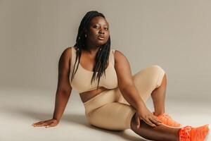 Young plus size African woman in sportswear looking confident while sitting against studio background photo