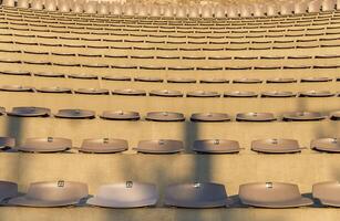 Rows of empty stadium seats, numbers visible, sunlight casting shadows, concert or sports event venue concept photo