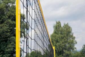 Volleyball net, outdoor scene with trees and sky in background, close-up view emphasizing sports equipment, sunny day concept photo