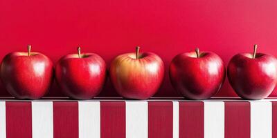 Row of vibrant red apples on striped surface against bold red background photo
