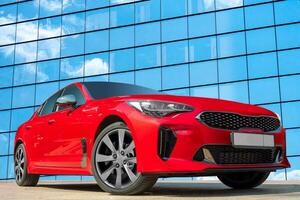 Red car on a background of a mirrored wall of a house with clouds reflections. Stylish, modern, bright image of the car for design solutions. photo