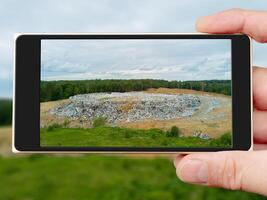 Garbage dump on smartphone screen. Polluting landfill in the forest. Problems of environmental pollution. photo