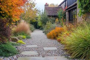 In this serene UK garden, hard landscaping is beautifully complemented by vibrant autumn colors. A charming pebbled path and diverse ornamental grasses enhance the natural beauty of the setting photo