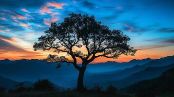 A beautiful silhouette of a majestic tree stands against a sunset, framed by distant mountains and clouds, creating a peaceful atmosphere that captivates the soul and invites reflection photo