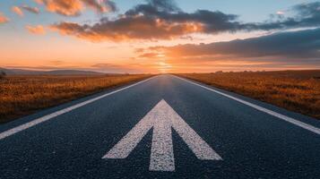 A scenic road stretches far into the horizon, beautifully marked by a clear arrow symbol, which signifies direction and progress as the vibrant sun sets peacefully behind the landscape photo