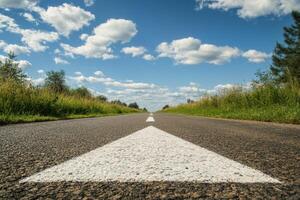 Picture an empty asphalt road stretching ahead, marked with a forward arrow, which symbolizes the essence of travel, progress, and fresh new beginnings, all beneath a serene blue sky overhead photo