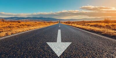 An empty, long asphalt road stretches out into the vast horizon, marked by a clear arrow that symbolizes both guidance and the continuous journey towards achieving success and reaching your goals photo