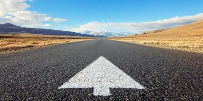 An expansive asphalt road stretches boldly ahead, marked by a prominent arrow pointing forward, representing the journey of direction, growth, and endless possibilities that lie on a clear horizon photo
