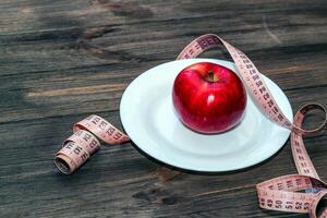 An apple on an empty white plate with a tape measure to measure the figure. Diet and raw food concept photo