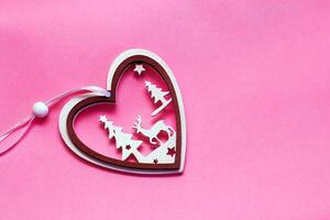 Wooden toy in the shape of a heart with winter ornament and a deer on a pink background. Home decor for the holiday photo