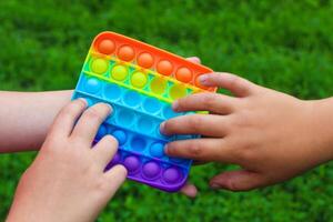 Child's hands are played square multicolored bubble toy antistress sensory pop it photo
