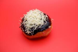 Donut cake with chocolate topping and grated cheese isolated on red background. photo