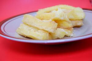 Fried cassava served on a plate. Fried cassava dish isolated on a red background. photo