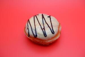 donut cake with white chocolate glaze topping and chocolate spread in zigzag pattern. donut cake isolated on red background. photo