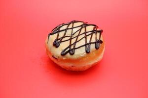 donut cake with white chocolate glaze topping and chocolate spread in zigzag pattern. donut cake isolated on red background. photo