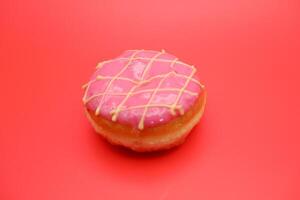 donut cake with pink chocolate glaze and white chocolate smeared in zigzag. donut cake isolated on red background. photo
