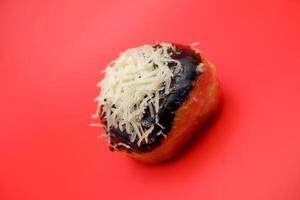 Donut cake with chocolate topping and grated cheese isolated on red background. photo