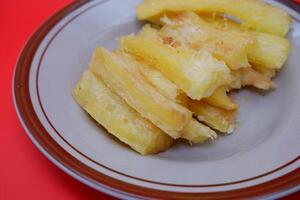 Fried cassava served on a plate. Fried cassava dish isolated on a red background. photo