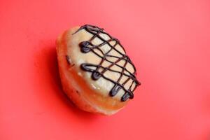 donut cake with white chocolate glaze topping and chocolate spread in zigzag pattern. donut cake isolated on red background. photo