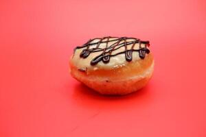 donut cake with white chocolate glaze topping and chocolate spread in zigzag pattern. donut cake isolated on red background. photo
