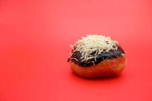Donut cake with chocolate topping and grated cheese isolated on red background. photo
