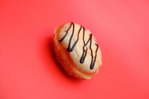 donut cake with white chocolate glaze topping and chocolate spread in zigzag pattern. donut cake isolated on red background. photo