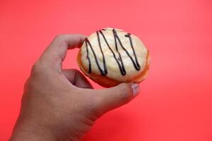 hand holding a donut cake isolated on red background. photo
