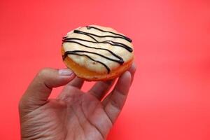 hand holding a donut cake isolated on red background. photo