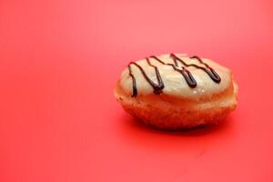 donut cake with white chocolate glaze topping and chocolate spread in zigzag pattern. donut cake isolated on red background. photo