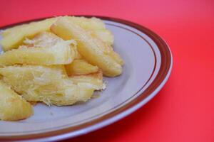Fried cassava served on a plate. Fried cassava dish isolated on a red background. photo
